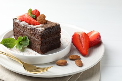 Photo of Piece of delicious chocolate cake with strawberries, almonds and mint on white table, closeup