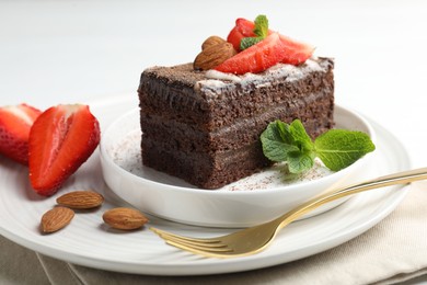 Photo of Piece of delicious chocolate cake with strawberries, almonds and mint on table, closeup