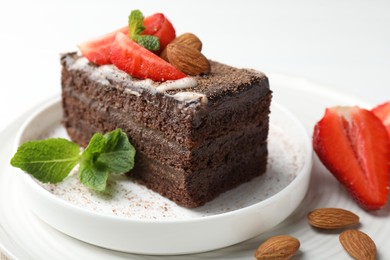 Photo of Piece of delicious chocolate cake with strawberries, almonds and mint on table, closeup