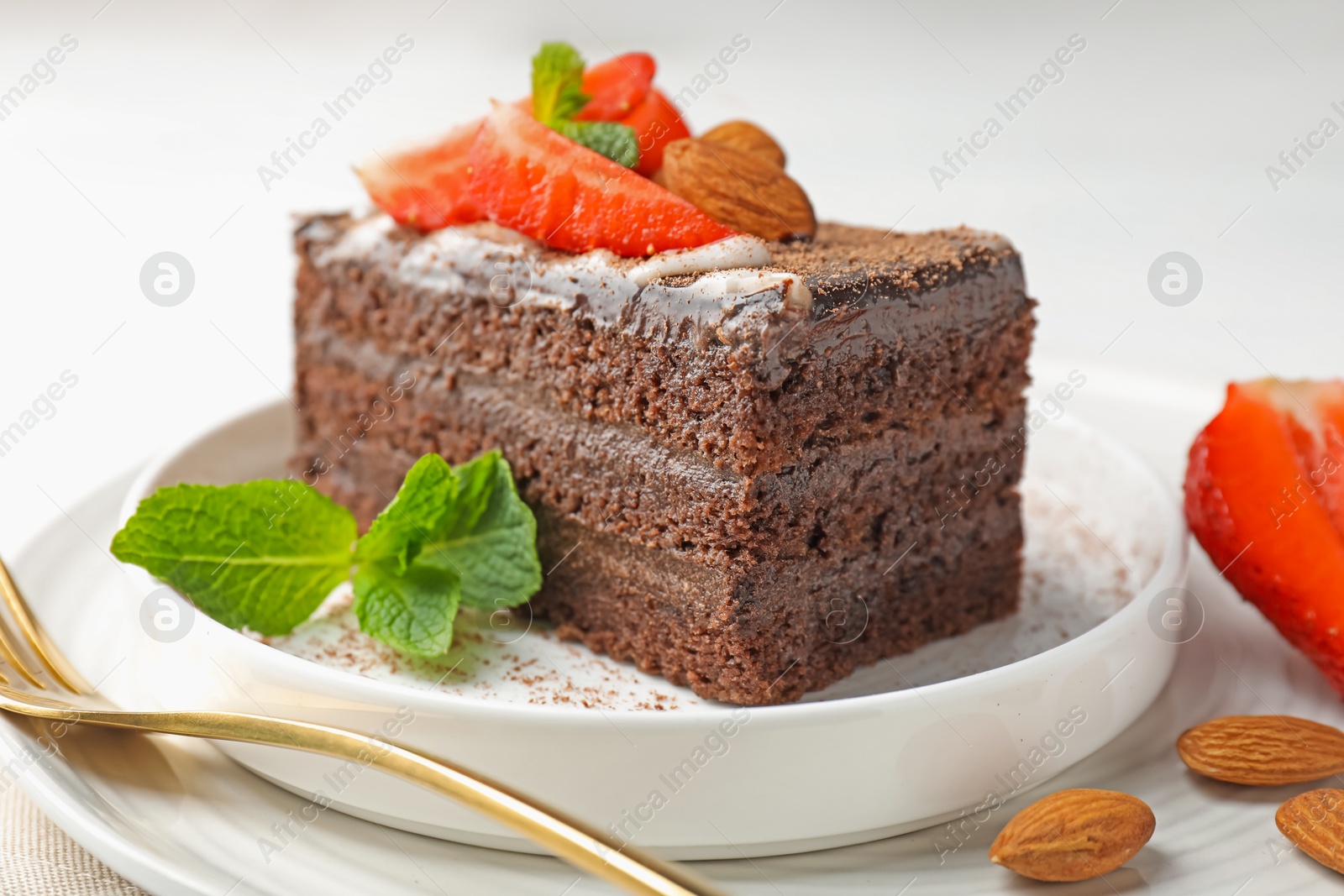 Photo of Piece of delicious chocolate cake with strawberry, almonds and mint on table, closeup