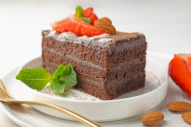 Photo of Piece of delicious chocolate cake with strawberry, almonds and mint on table, closeup
