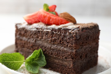 Photo of Piece of delicious chocolate cake with strawberry, almonds and mint on table, closeup
