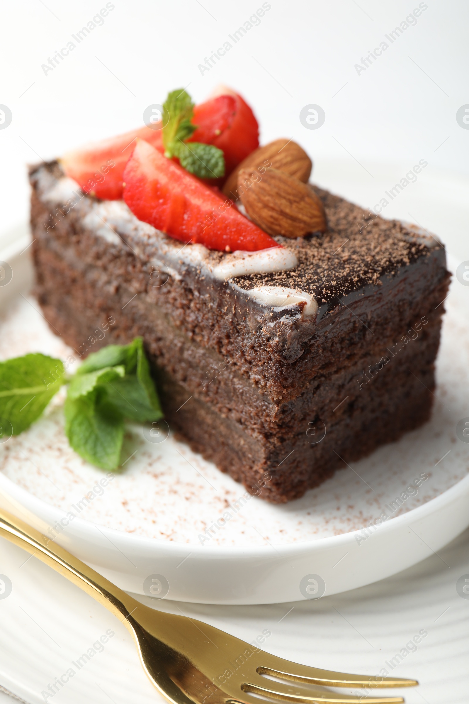 Photo of Piece of delicious chocolate cake with strawberry, almonds and mint on table, closeup
