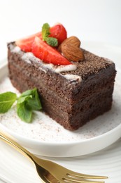 Photo of Piece of delicious chocolate cake with strawberry, almonds and mint on table, closeup