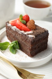 Photo of Piece of delicious chocolate cake with strawberry, almonds, mint and tea on table, closeup