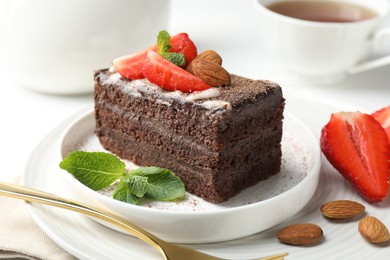 Photo of Piece of delicious chocolate cake with strawberry, almonds, mint and tea on table, closeup