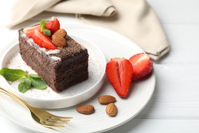 Photo of Piece of delicious chocolate cake with strawberries, almonds and mint on white wooden table, closeup
