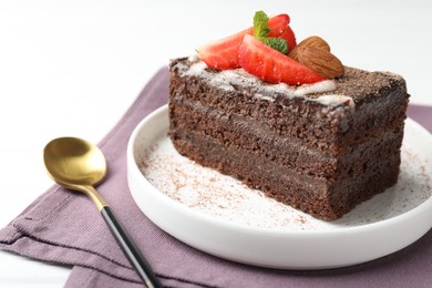 Photo of Piece of delicious chocolate cake with strawberry, almonds and mint on table, closeup