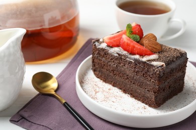 Photo of Piece of delicious chocolate cake with strawberry, almonds and tea on table, closeup