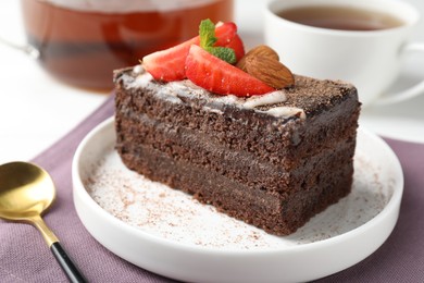 Photo of Piece of delicious chocolate cake with strawberry, almonds and tea on table, closeup