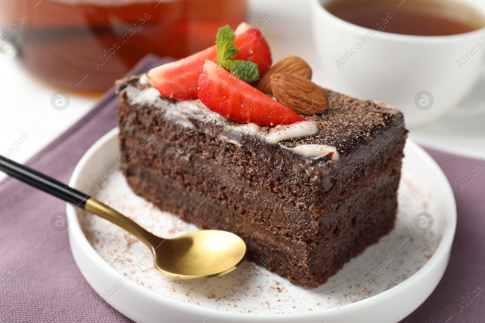 Photo of Piece of delicious chocolate cake with strawberry, almonds and tea on table, closeup