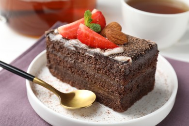Photo of Piece of delicious chocolate cake with strawberry, almonds and tea on table, closeup
