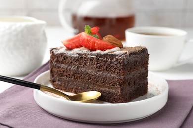 Photo of Piece of delicious chocolate cake with strawberry, almonds and tea on table, closeup