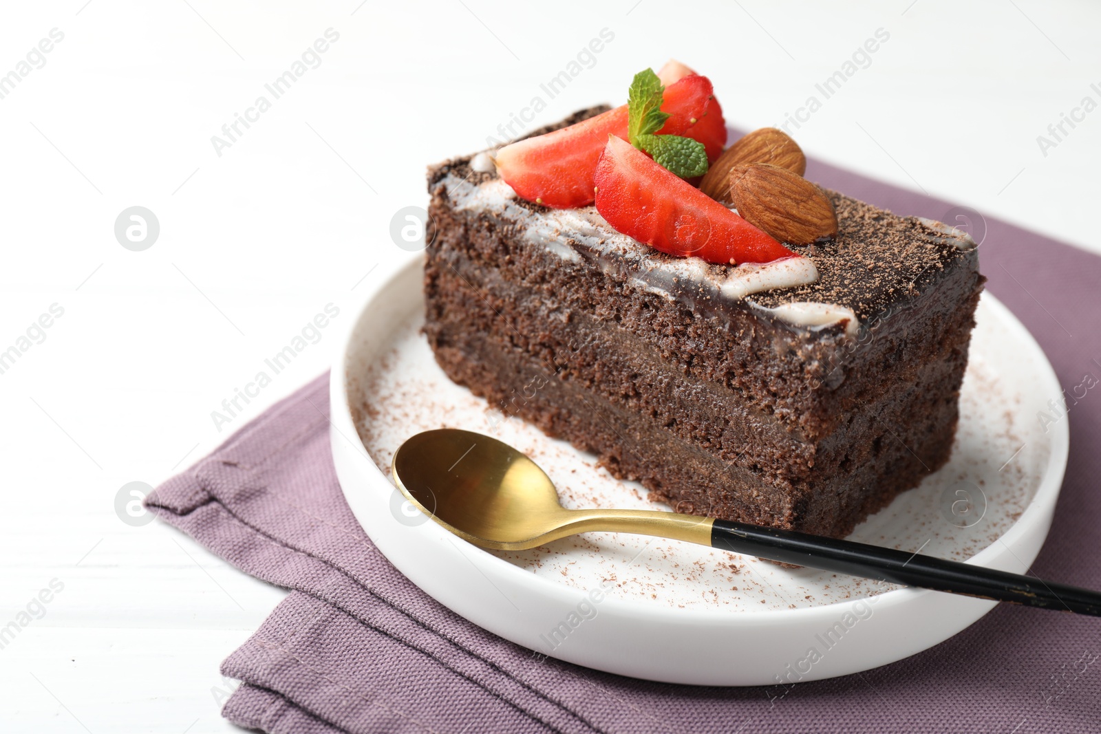 Photo of Piece of delicious chocolate cake with strawberry and almonds on white table, closeup. Space for text