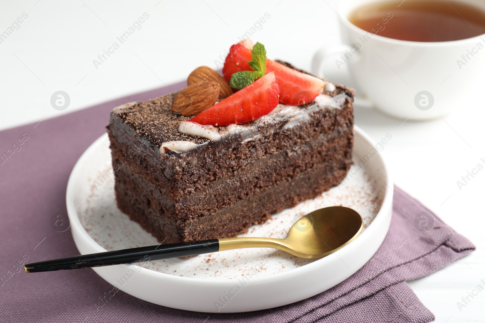 Piece of delicious chocolate cake with strawberry, almonds and tea on white table, closeup Photo of Piece of delicious chocolate cake with strawberry, almonds and tea on white table, closeup