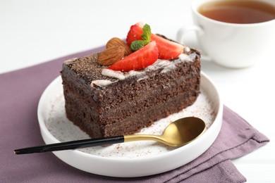 Photo of Piece of delicious chocolate cake with strawberry, almonds and tea on white table, closeup