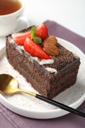 Photo of Piece of delicious chocolate cake with strawberry, almonds and tea on table, closeup