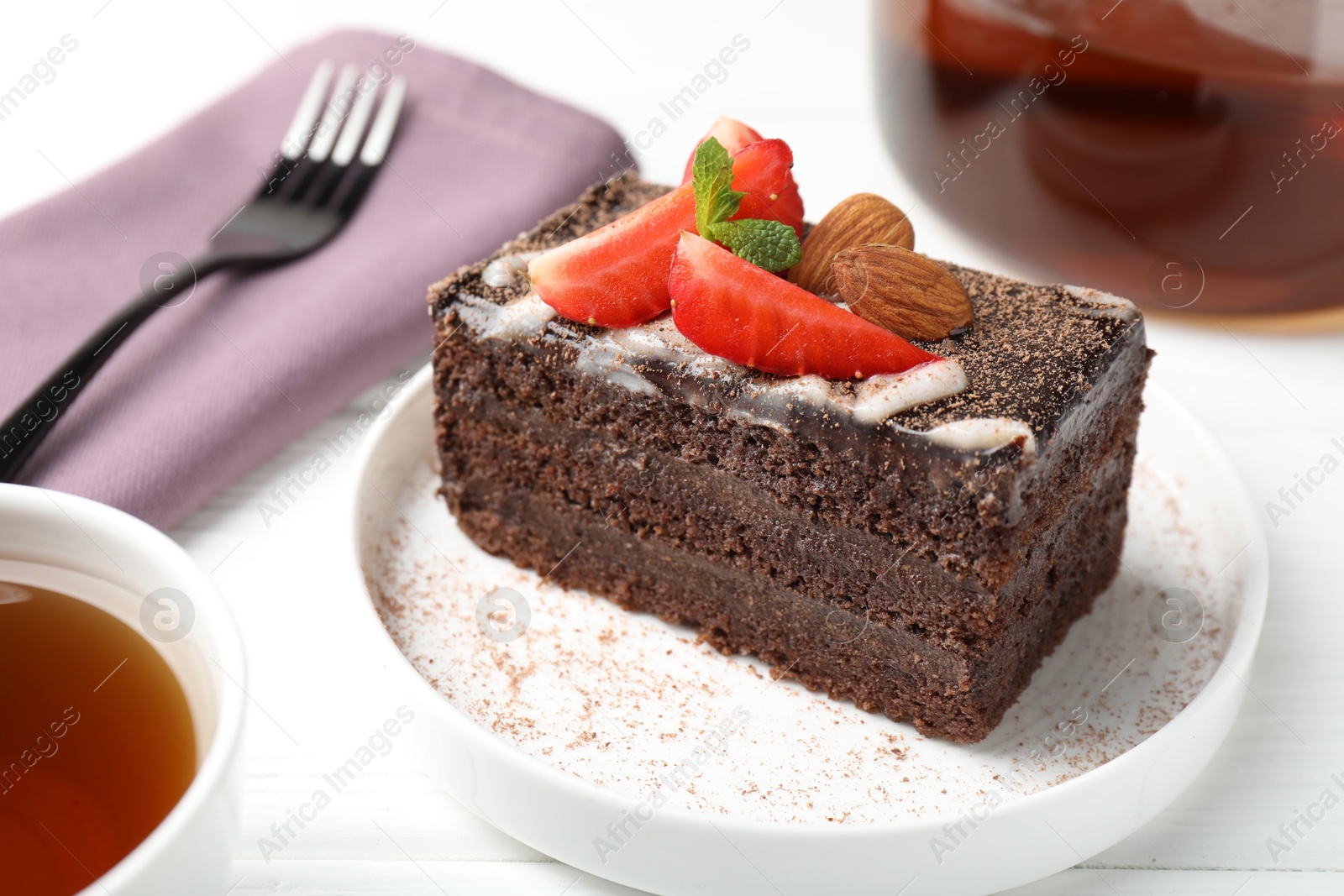 Photo of Piece of delicious chocolate cake with strawberry, almonds and tea on white wooden table, closeup