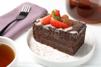 Photo of Piece of delicious chocolate cake with strawberry, almonds and tea on white wooden table, closeup