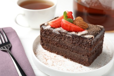 Photo of Piece of delicious chocolate cake with strawberry, almonds and tea on white table, closeup