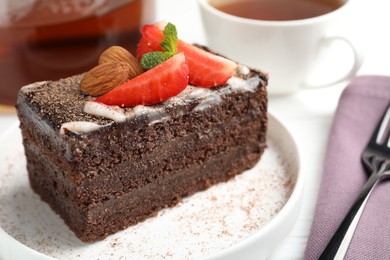 Photo of Piece of delicious chocolate cake with strawberry, almonds and tea on table, closeup