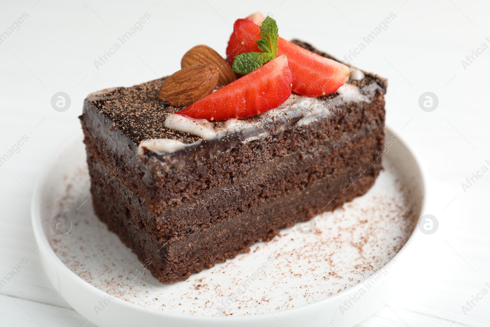 Piece of delicious chocolate cake with strawberry and almonds on white table, closeup Photo of Piece of delicious chocolate cake with strawberry and almonds on white table, closeup