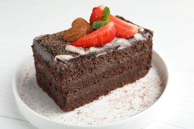 Photo of Piece of delicious chocolate cake with strawberry and almonds on white table, closeup