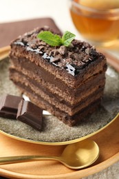 Photo of Piece of delicious chocolate cake with mint and tea on table, closeup