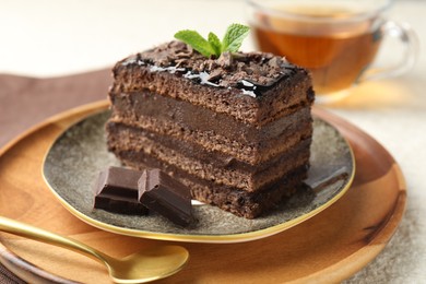Photo of Piece of delicious chocolate cake with mint and tea on table, closeup
