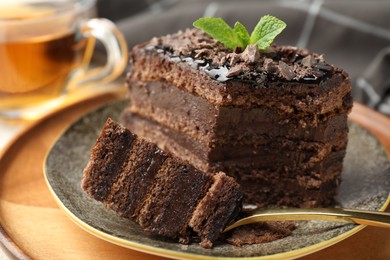 Photo of Piece of delicious chocolate cake with mint and tea on table, closeup