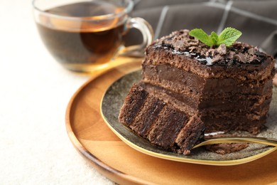 Photo of Piece of delicious chocolate cake with mint and tea on white table, closeup. Space for text