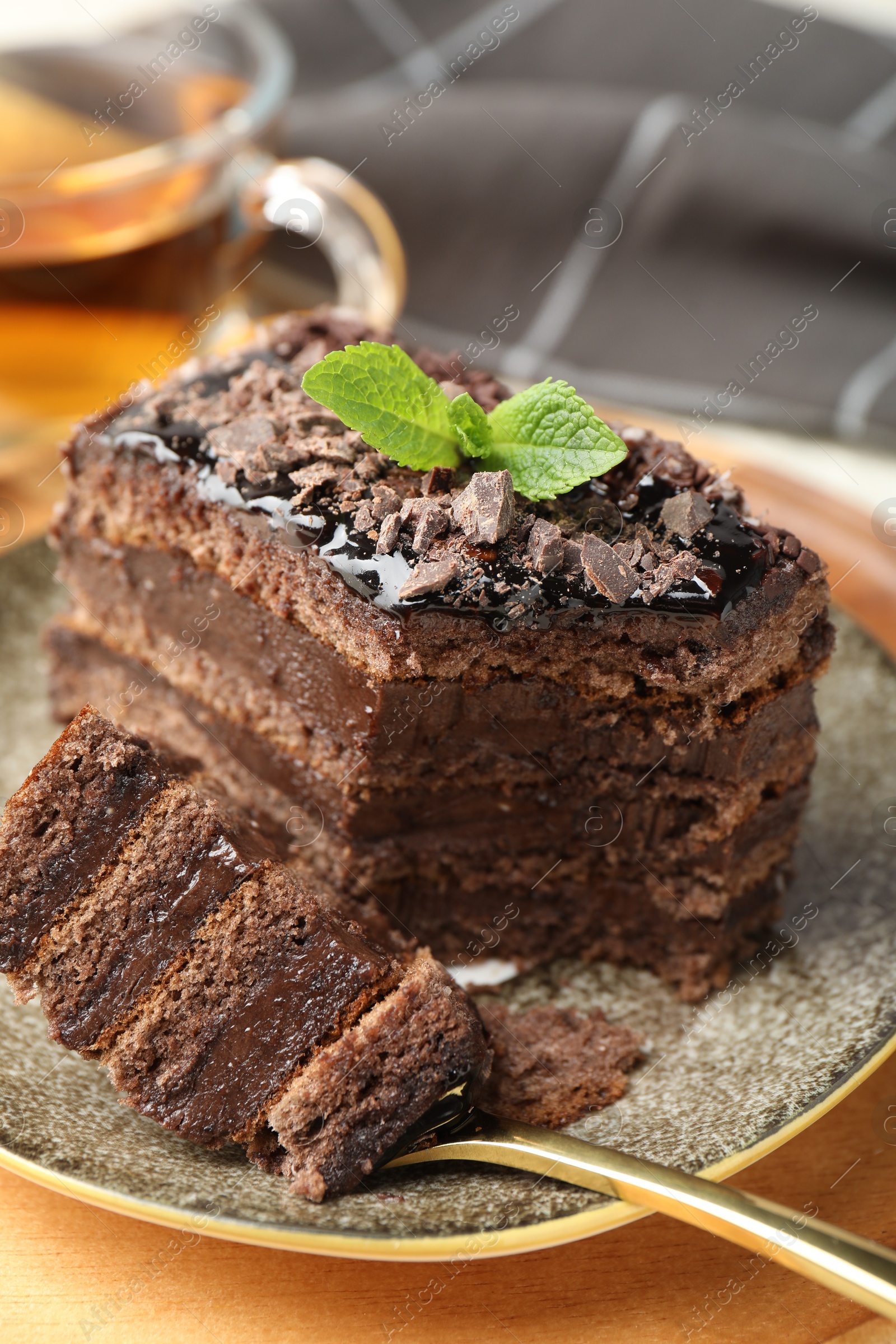 Photo of Piece of delicious chocolate cake with mint and tea on table, closeup