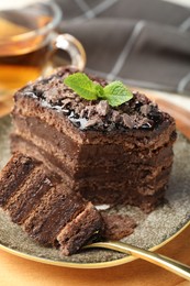 Photo of Piece of delicious chocolate cake with mint and tea on table, closeup