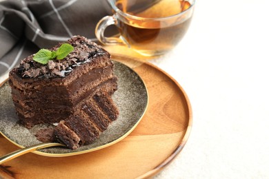 Photo of Piece of delicious chocolate cake with mint and tea on white table, closeup. Space for text