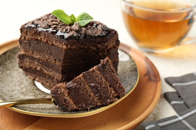 Photo of Piece of delicious chocolate cake with mint and tea on table, closeup