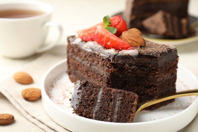 Photo of Piece of delicious chocolate cake with strawberry, almonds and tea on table, closeup