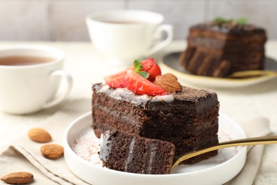 Photo of Piece of delicious chocolate cake with strawberry, almonds and tea on table, closeup