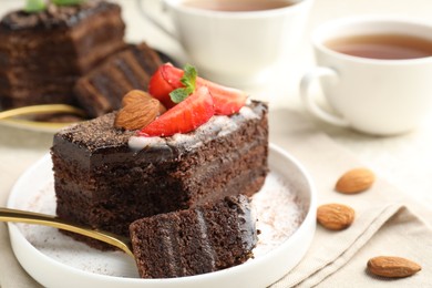 Photo of Piece of delicious chocolate cake with strawberry, almonds and tea on table, closeup