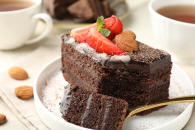 Photo of Piece of delicious chocolate cake with strawberry, almonds and tea on table, closeup