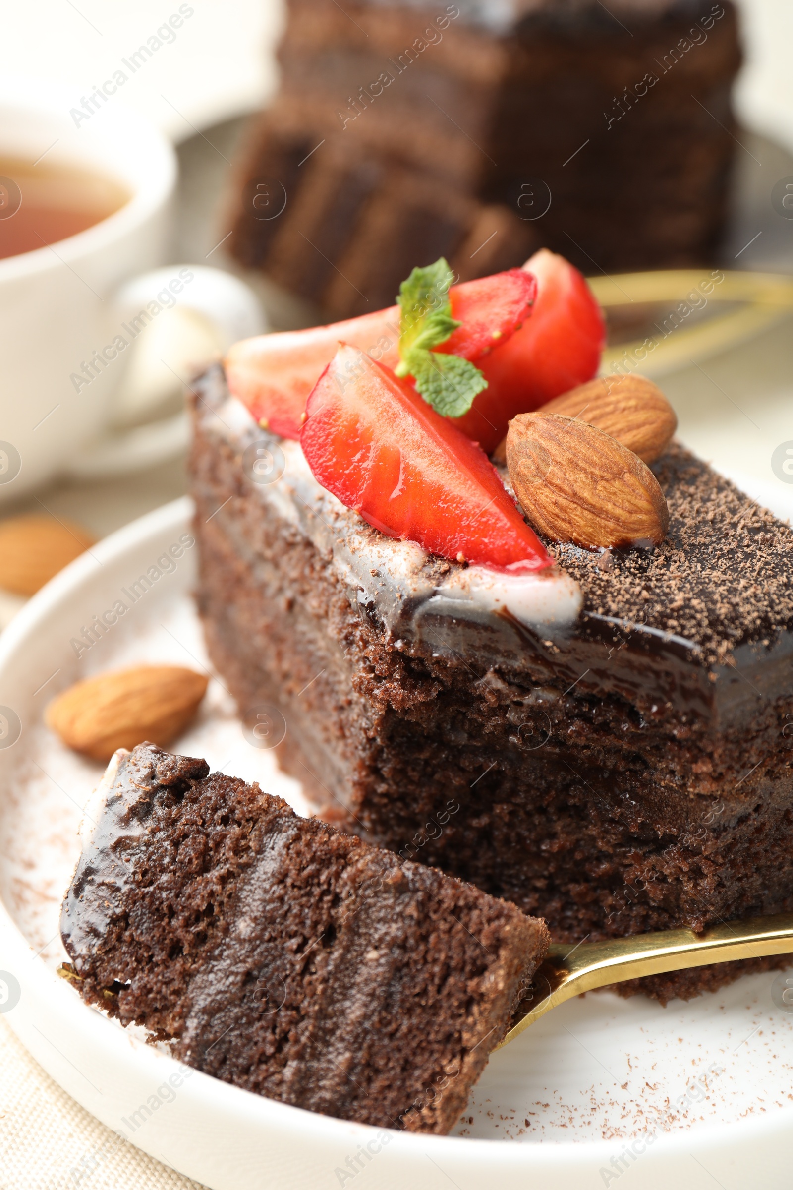 Photo of Piece of delicious chocolate cake with strawberry and almonds on table, closeup