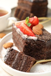 Photo of Piece of delicious chocolate cake with strawberry and almonds on table, closeup
