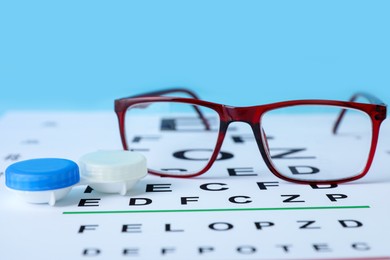 Photo of Glasses, vision test chart and lenses on light blue background, closeup