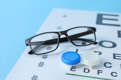 Photo of Glasses, vision test chart and lenses on light blue background, closeup