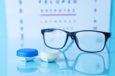 Photo of Glasses, vision test chart and lenses on light blue background, selective focus
