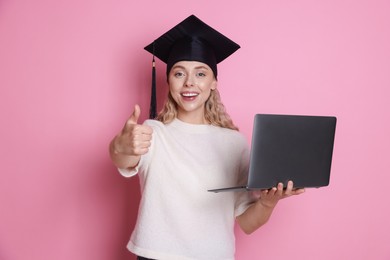 Photo of Happy student with laptop showing thumbs up after graduation on pink background