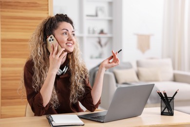 Photo of Smiling woman talking by smartphone at desk with laptop in home office