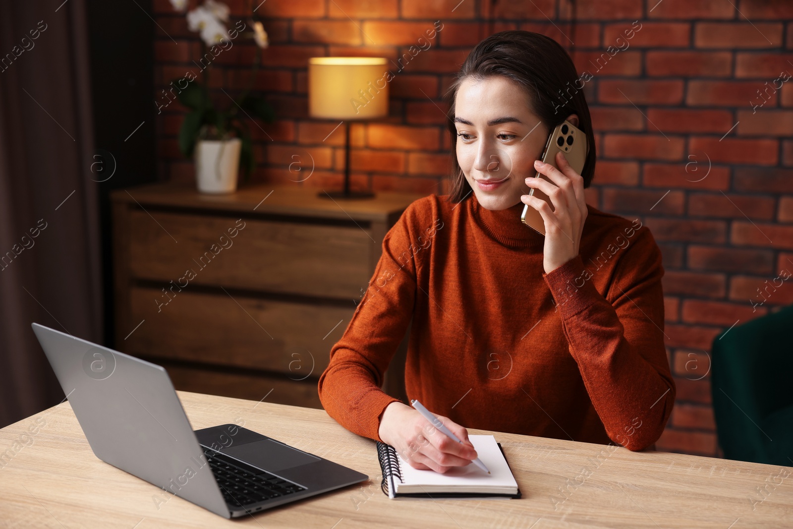 Woman talking by smartphone and working at desk in home office Photo of Woman talking by smartphone and working at desk in home office