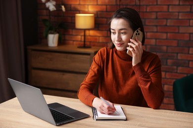 Photo of Woman talking by smartphone and working at desk in home office