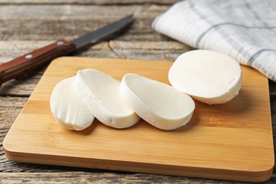 Photo of Cut mozzarella cheese and knife on wooden table, closeup
