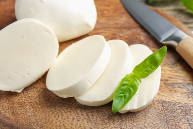 Photo of Cut mozzarella cheese with basil and knife on wooden table, closeup